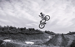 Schwarz-Weiß-Aufnahme von BMX-Freestyle-Fahrer bei einem Dirt-Jump in großer Höhe